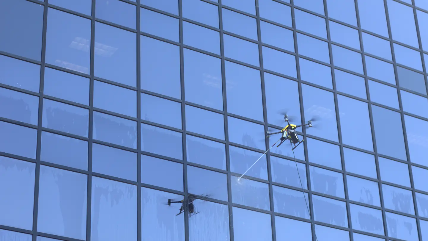 A cleaning drone on a tether sprays the glass panels of a tall office building