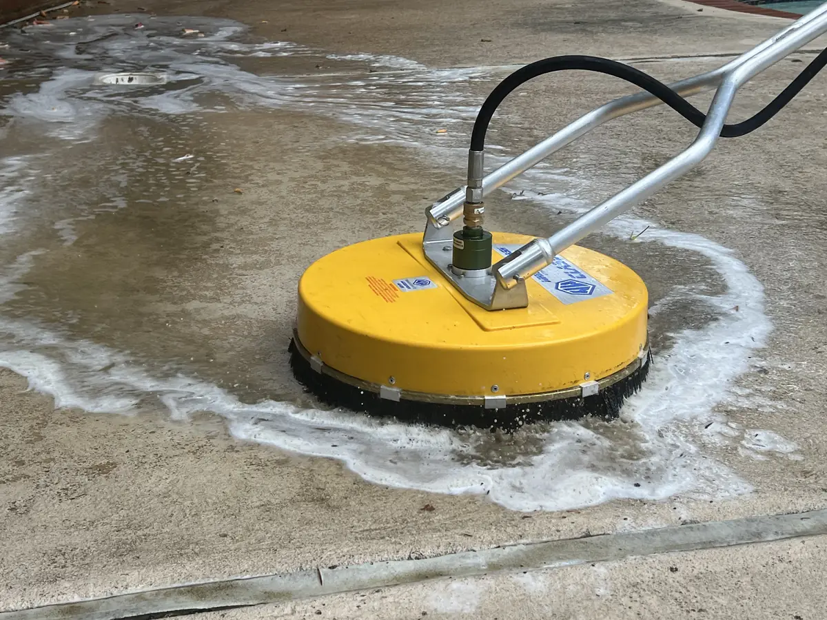 A surface cleaner moves across a wet concrete deck and leaves a cleaner path behind it