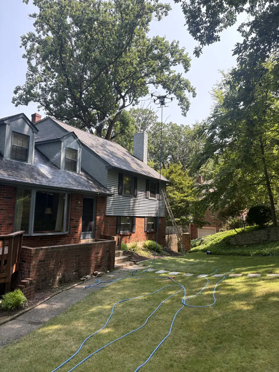 A cleaning drone above a brick and siding house with a hose that runs to the truck