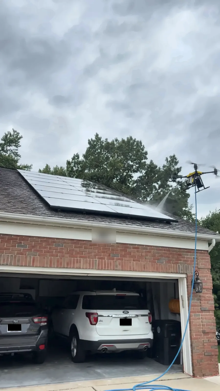 Drone solar panel cleaning on a rooftop array above a brick garage